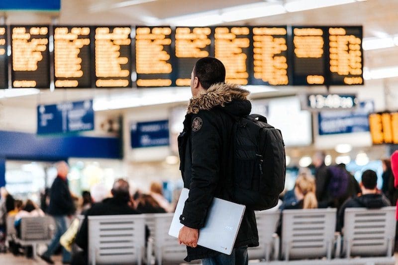 Young man looking at flight roster at airport wearing winter coat