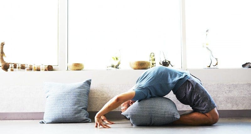 man doing yoga at home using pillow for back support