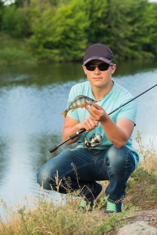 man with baseball cap holding fish and fishing pole