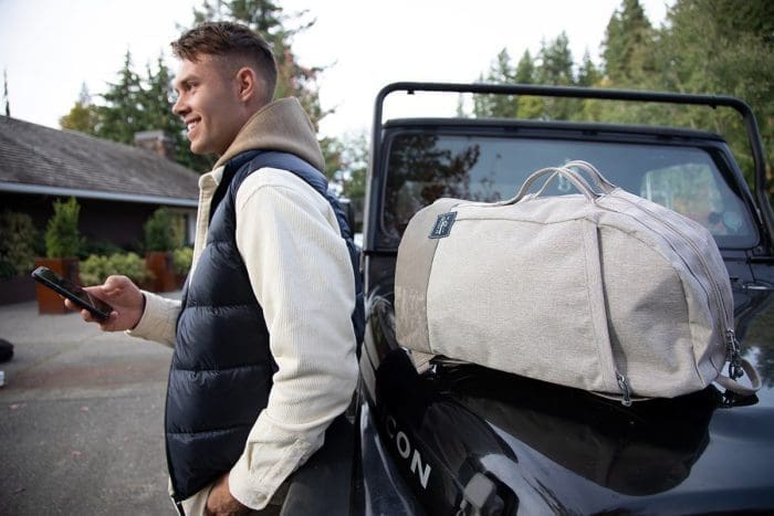 man with duffle bag outside on top of vehicle