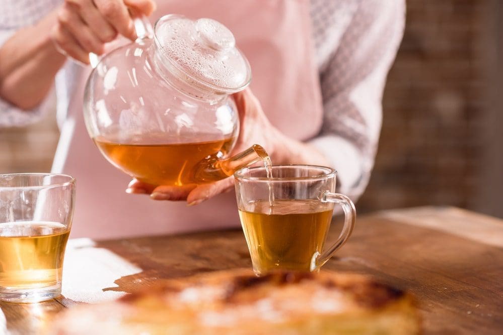 woman pouring hot tea clear glass container