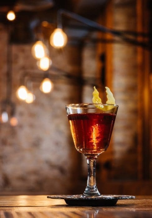 Close-up view of alcoholic sazerac cocktail in glass on wooden table-min