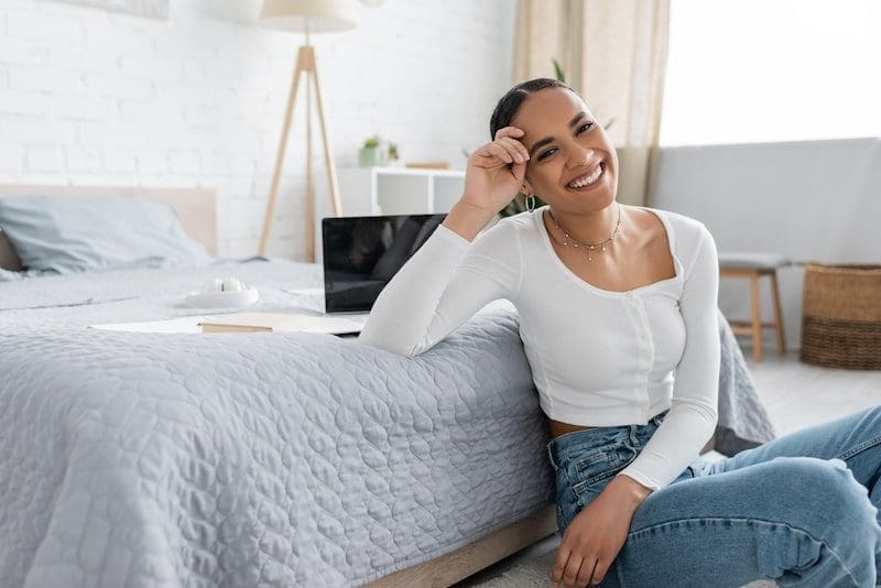 Charming african american student smiling while sitting near laptop