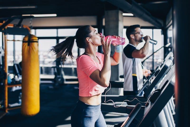 Young fit man and woman running on treadmill