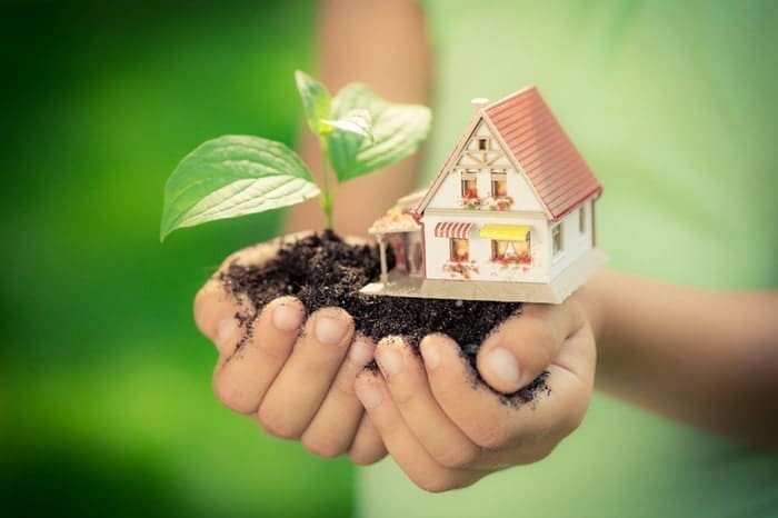 Young child holding a small house in the dirt, eco-friendly