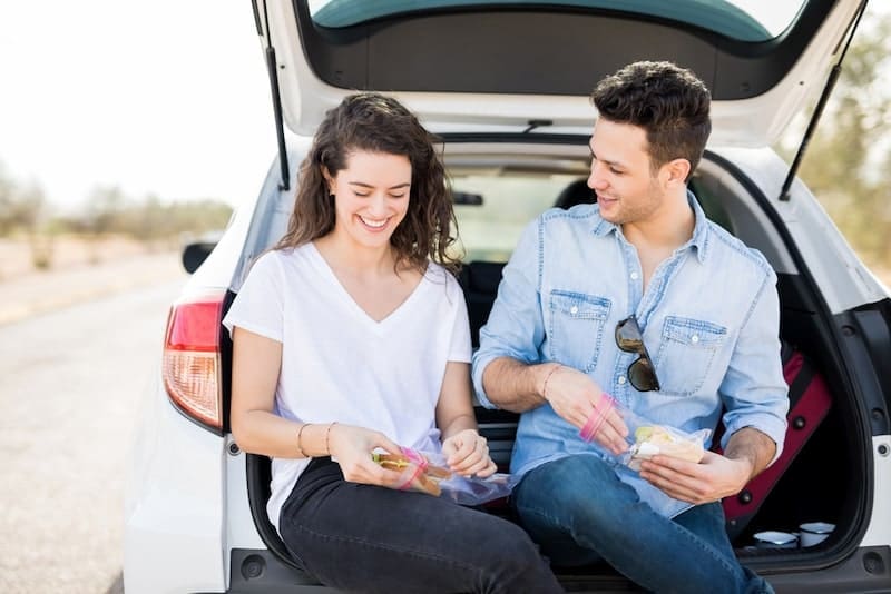 Couple sitting together in trunk of car and eating sandwich
