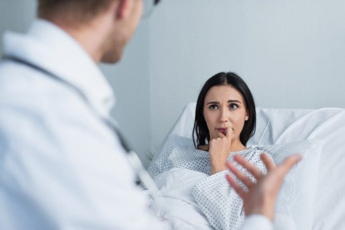 Brunette woman in patient gown looking at blurred doctor in hospital