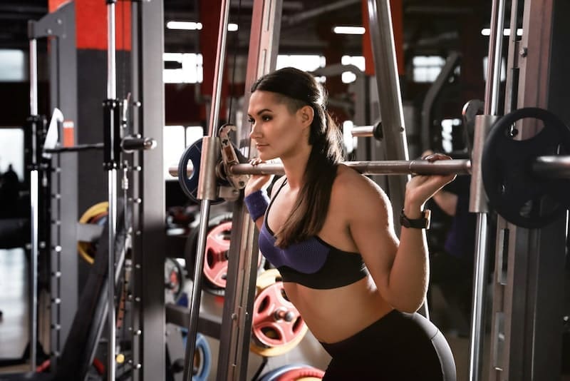 Young woman working out on Smith machine in modern gym-min